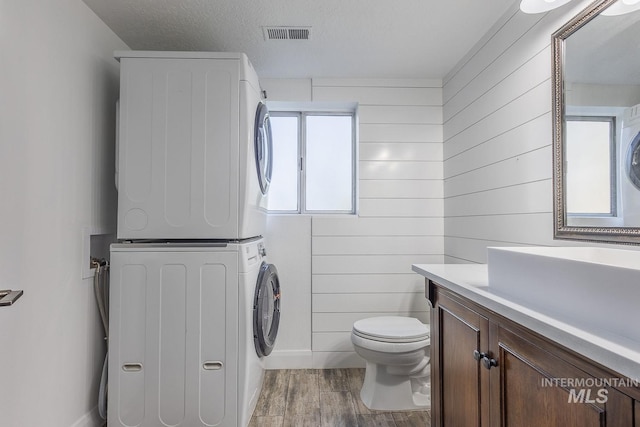 bathroom featuring hardwood / wood-style floors, a textured ceiling, stacked washer / drying machine, toilet, and vanity