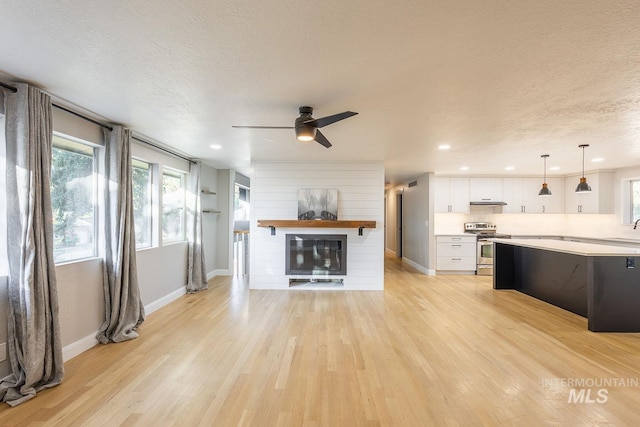 unfurnished living room with a textured ceiling, ceiling fan, sink, a fireplace, and light hardwood / wood-style floors