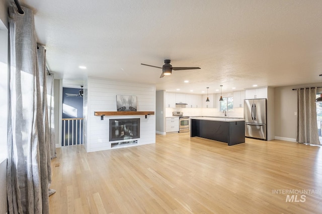 unfurnished living room with a textured ceiling, a large fireplace, ceiling fan, sink, and light hardwood / wood-style floors