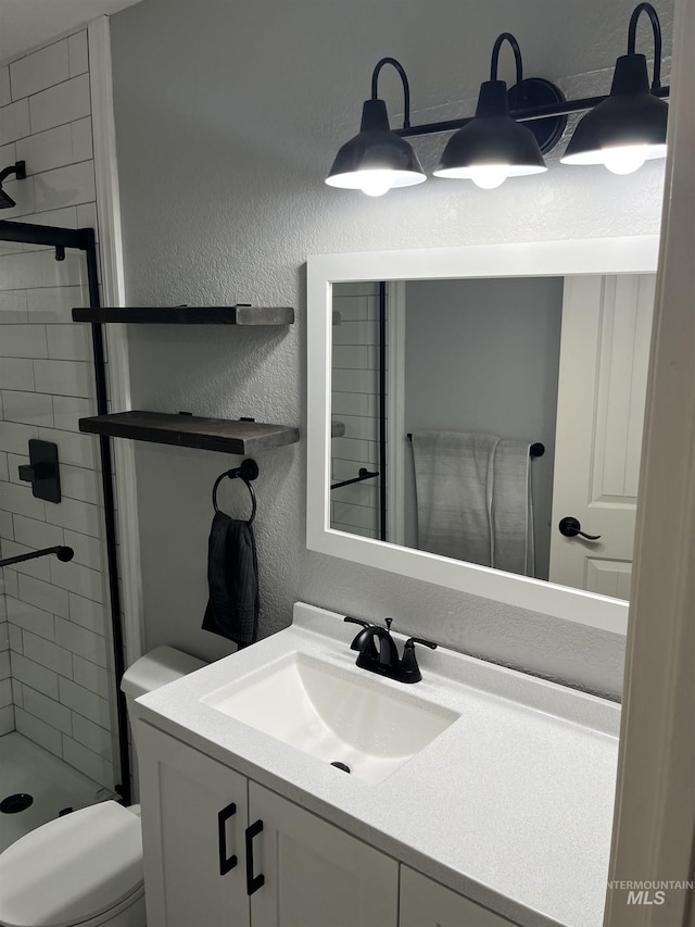 bathroom with vanity, toilet, and tiled shower