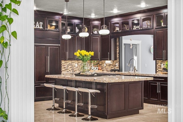 bar with light stone countertops, sink, dark brown cabinets, and pendant lighting