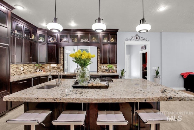 kitchen featuring a kitchen island with sink, sink, and decorative light fixtures