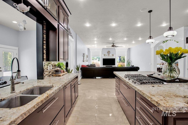 kitchen with sink, ceiling fan, hanging light fixtures, light stone counters, and decorative backsplash