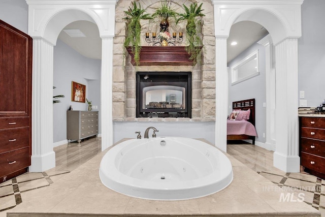 bathroom with a relaxing tiled tub, vanity, and a multi sided fireplace