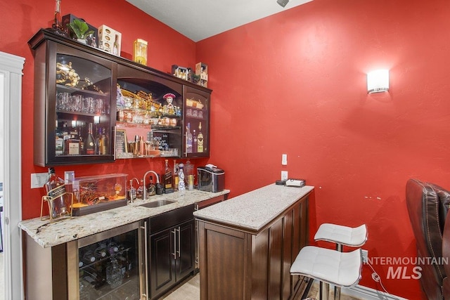 bar with wine cooler, light stone countertops, sink, and dark brown cabinets