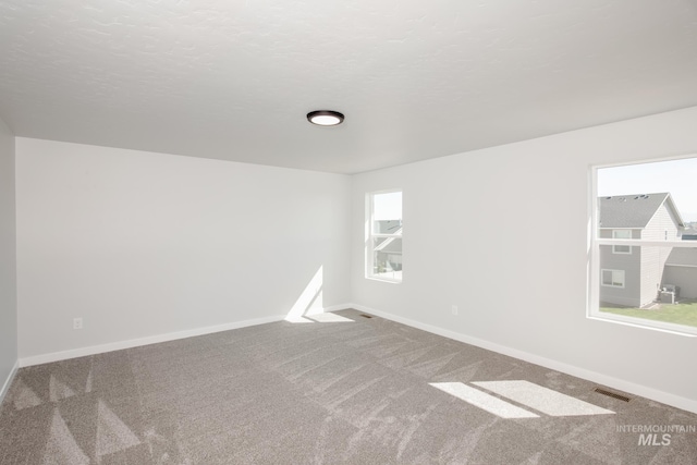 carpeted empty room featuring baseboards, visible vents, and a textured ceiling