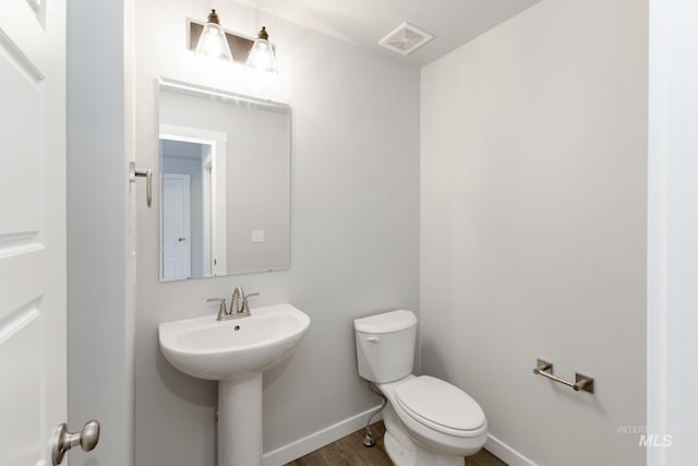 bathroom with visible vents, toilet, a sink, wood finished floors, and baseboards