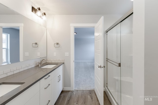 full bath with double vanity, wood finished floors, a stall shower, and a sink