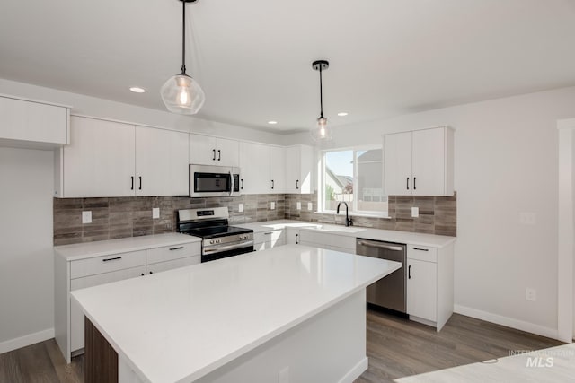 kitchen with stainless steel appliances, backsplash, a kitchen island, a sink, and wood finished floors