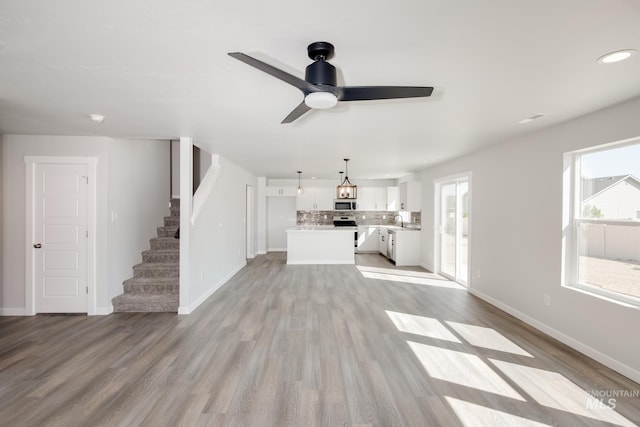 unfurnished living room featuring light wood-type flooring, a sink, stairway, and baseboards