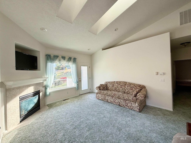 living room with carpet floors, a tiled fireplace, a textured ceiling, and lofted ceiling with skylight