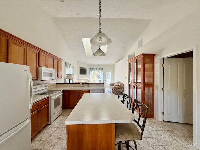 kitchen with a center island, a breakfast bar, white appliances, sink, and decorative light fixtures