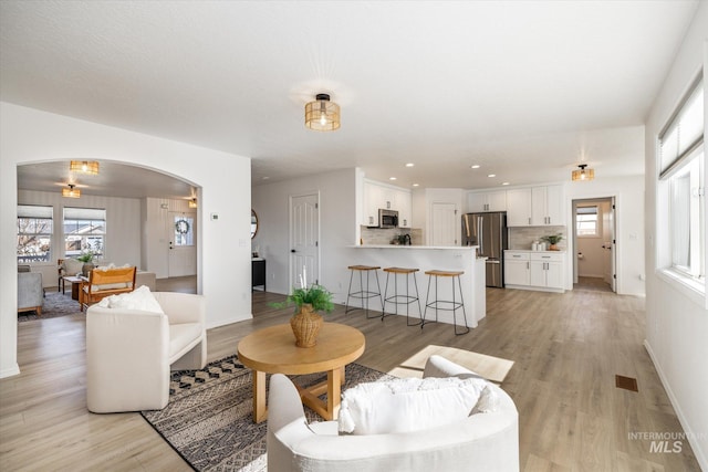 living room featuring visible vents, baseboards, light wood-style flooring, recessed lighting, and arched walkways