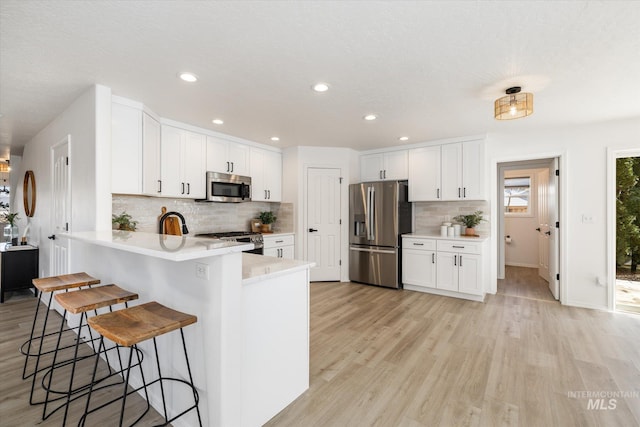 kitchen with a kitchen breakfast bar, appliances with stainless steel finishes, a peninsula, light wood finished floors, and light countertops