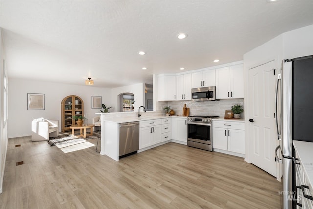 kitchen with a peninsula, arched walkways, a sink, white cabinets, and appliances with stainless steel finishes