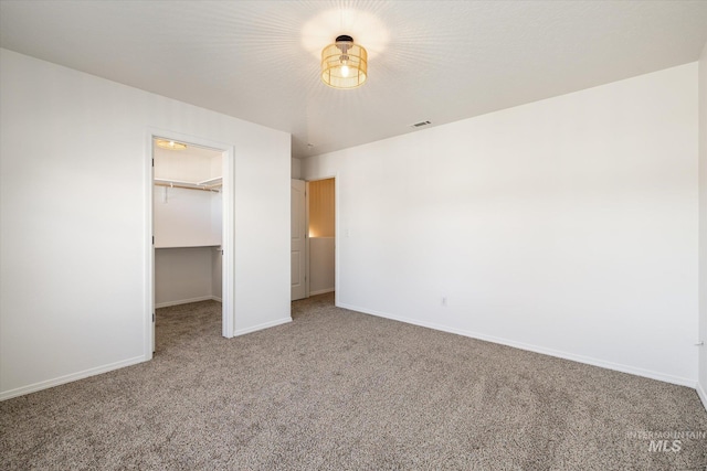 unfurnished bedroom with a walk in closet, visible vents, a closet, carpet floors, and baseboards