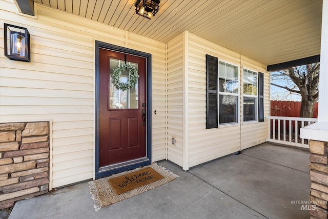 doorway to property with a porch and fence