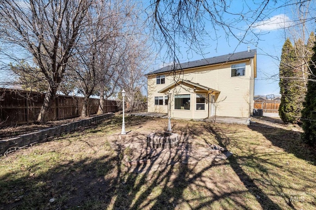 back of house featuring central air condition unit, a fenced backyard, a lawn, and an outdoor fire pit