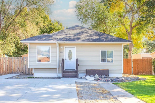 bungalow-style house with entry steps, a front lawn, roof with shingles, and fence