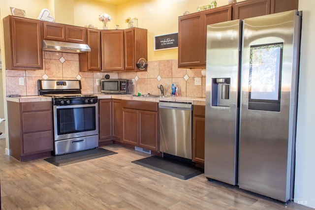 kitchen featuring light wood-style flooring, a sink, stainless steel appliances, tile counters, and under cabinet range hood