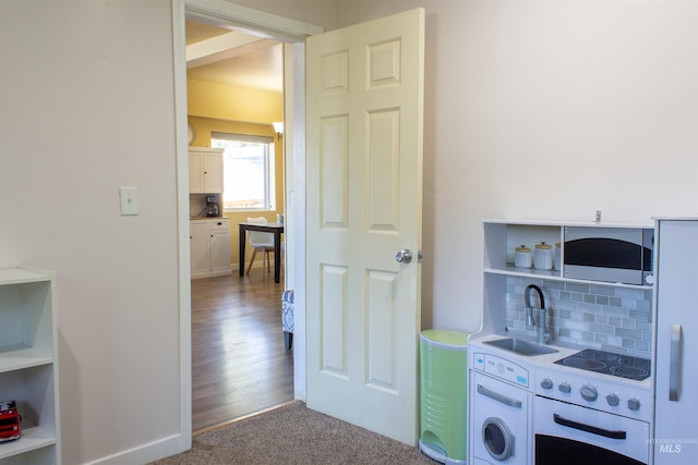 kitchen featuring open shelves, a sink, backsplash, light countertops, and black electric stovetop