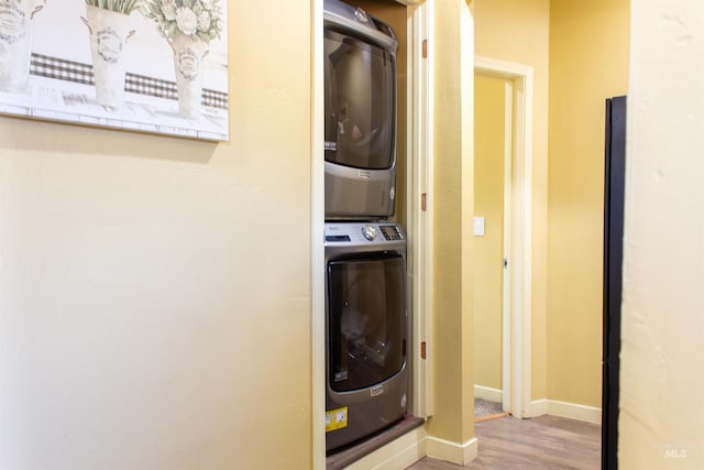 laundry area featuring stacked washer / dryer, wood finished floors, and baseboards