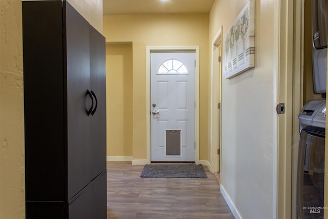 foyer with stacked washer / drying machine, baseboards, and wood finished floors