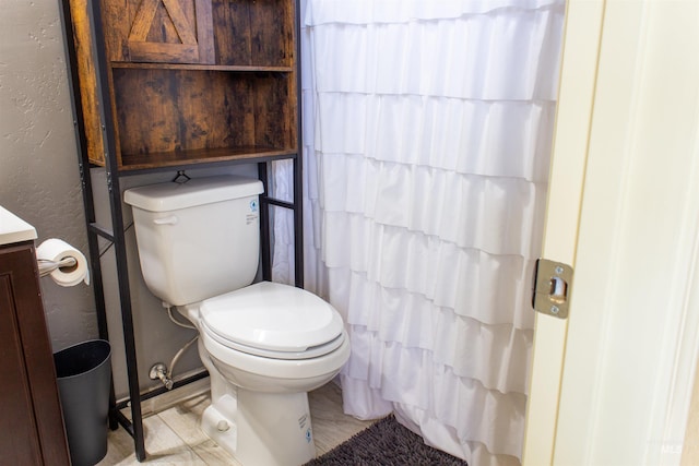 full bathroom featuring toilet, vanity, and a textured wall