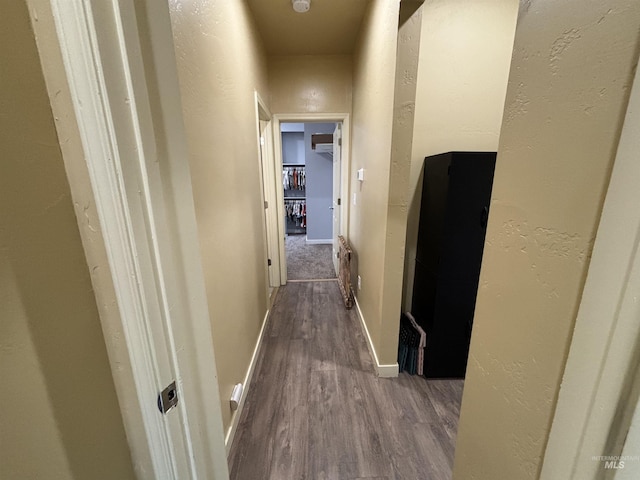 hallway with dark wood-type flooring, baseboards, and a textured wall