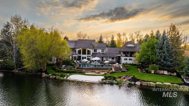 1122 W Two Rivers Ln, Eagle, ID 83616 - back of property at dusk featuring a balcony, a lawn, a pool, and a water view