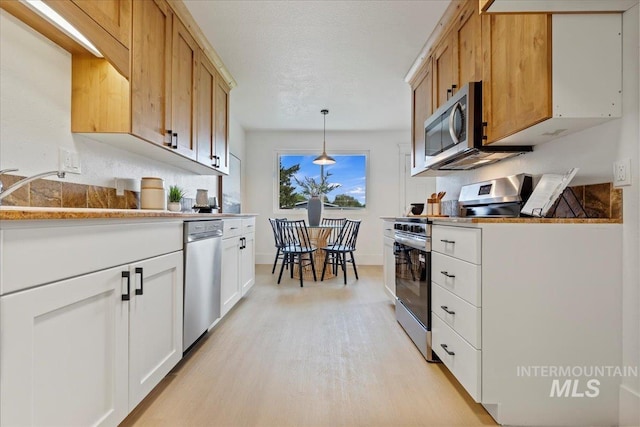 kitchen featuring decorative light fixtures, light countertops, white cabinets, light wood finished floors, and stainless steel appliances