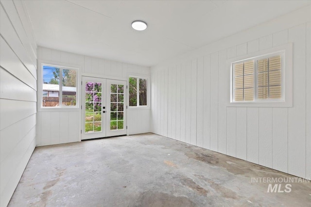 spare room featuring french doors, concrete flooring, and wooden walls