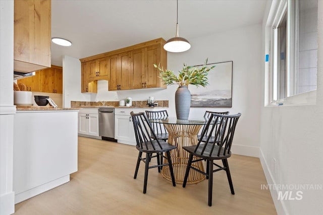 kitchen with stainless steel dishwasher, pendant lighting, baseboards, light countertops, and light wood-style flooring