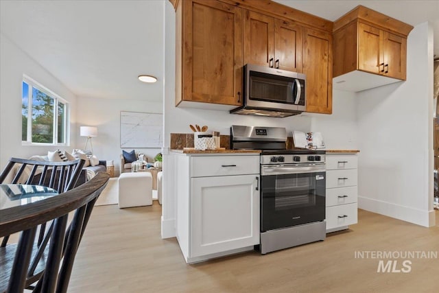 kitchen featuring brown cabinets, baseboards, open floor plan, stainless steel appliances, and light wood-style flooring