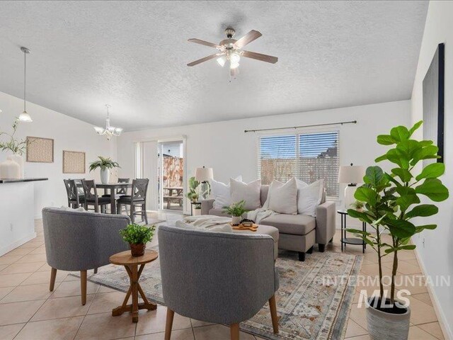 living area featuring light tile patterned flooring, ceiling fan with notable chandelier, baseboards, and a textured ceiling