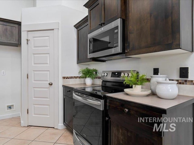kitchen featuring baseboards, dark brown cabinetry, light countertops, light tile patterned flooring, and stainless steel appliances