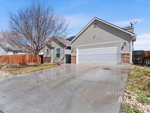 single story home featuring fence, concrete driveway, a garage, stone siding, and roof mounted solar panels