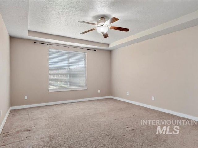 carpeted empty room with a tray ceiling, baseboards, a textured ceiling, and a ceiling fan