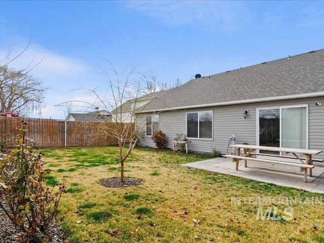 back of property with a patio, a lawn, roof with shingles, and fence