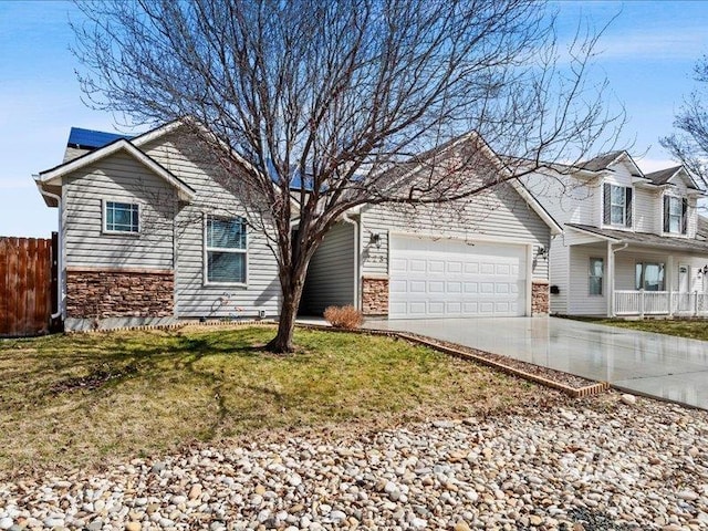 view of front facade featuring fence, concrete driveway, a front yard, stone siding, and an attached garage