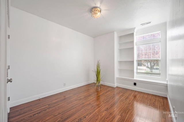 spare room with built in shelves, baseboards, wood finished floors, and visible vents