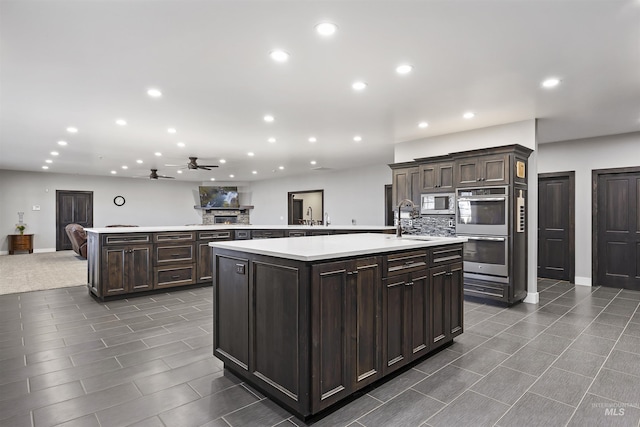 kitchen featuring a sink, a large island, light countertops, appliances with stainless steel finishes, and tasteful backsplash