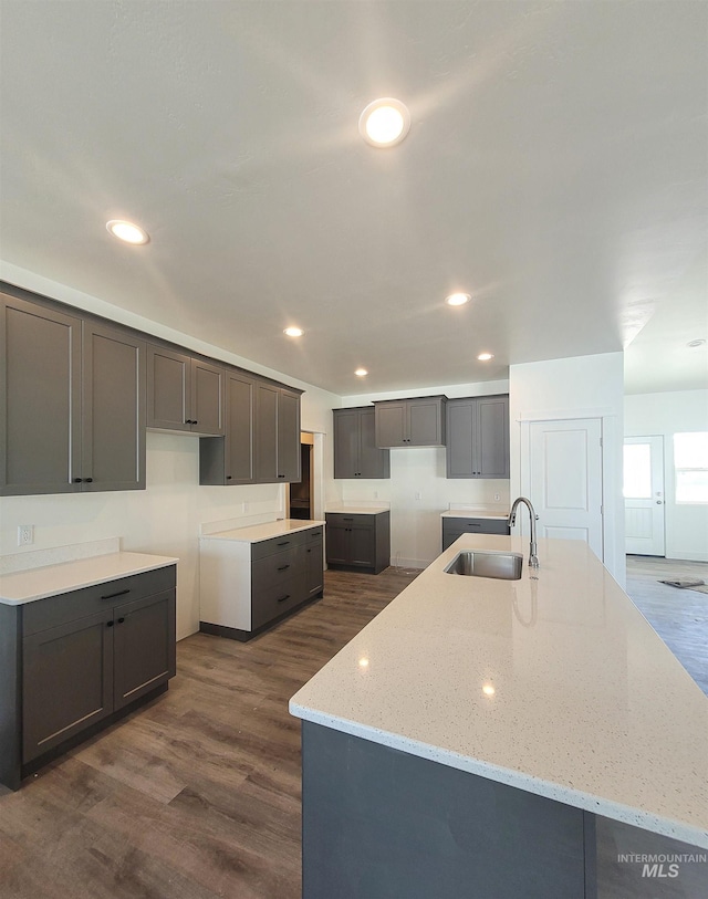 kitchen with a center island with sink, dark hardwood / wood-style floors, light stone countertops, and sink