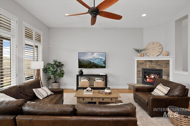 living room featuring recessed lighting, a ceiling fan, a stone fireplace, wood finished floors, and baseboards