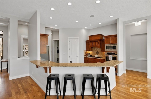 kitchen with appliances with stainless steel finishes, brown cabinetry, backsplash, and a kitchen breakfast bar