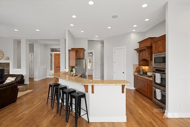 kitchen featuring appliances with stainless steel finishes, a peninsula, a breakfast bar area, and light wood finished floors