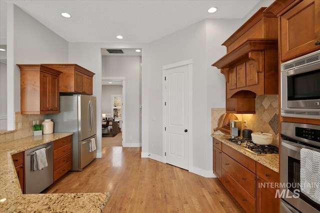 kitchen featuring stainless steel appliances, brown cabinetry, visible vents, and light wood finished floors