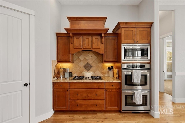 kitchen with light wood finished floors, appliances with stainless steel finishes, brown cabinetry, and backsplash