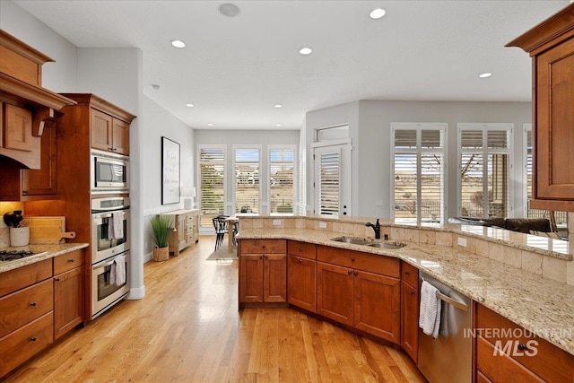 kitchen with light wood-style flooring, appliances with stainless steel finishes, brown cabinetry, and a sink