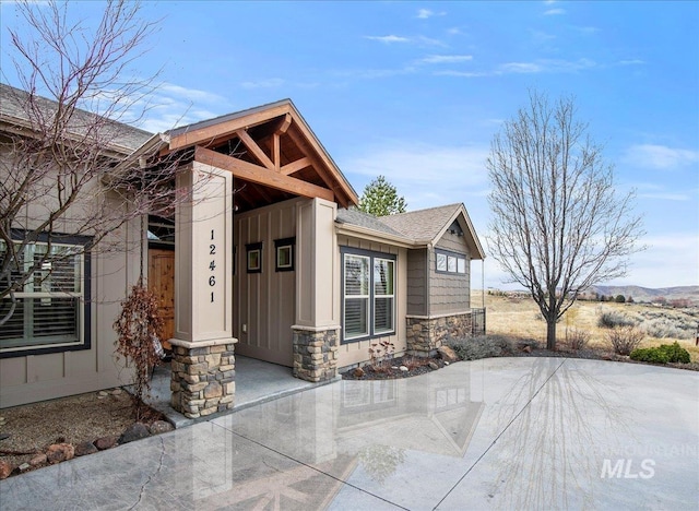 property entrance featuring stone siding, board and batten siding, and roof with shingles